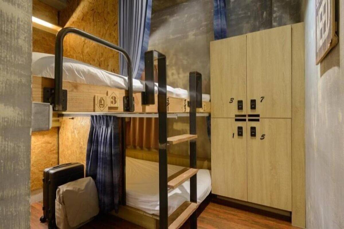 Quarto com beliche de madeira, guarda-roupa com divisórias numeradas e uma mala no chão.