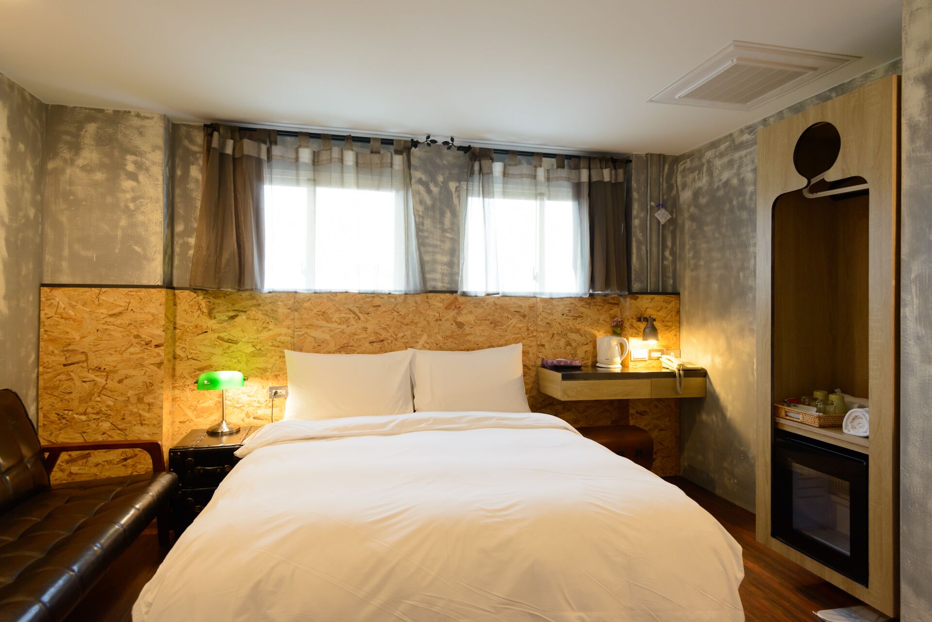 A hotel room with a bed, a desk with a lamp, a chair, a wardrobe, and a fireplace.