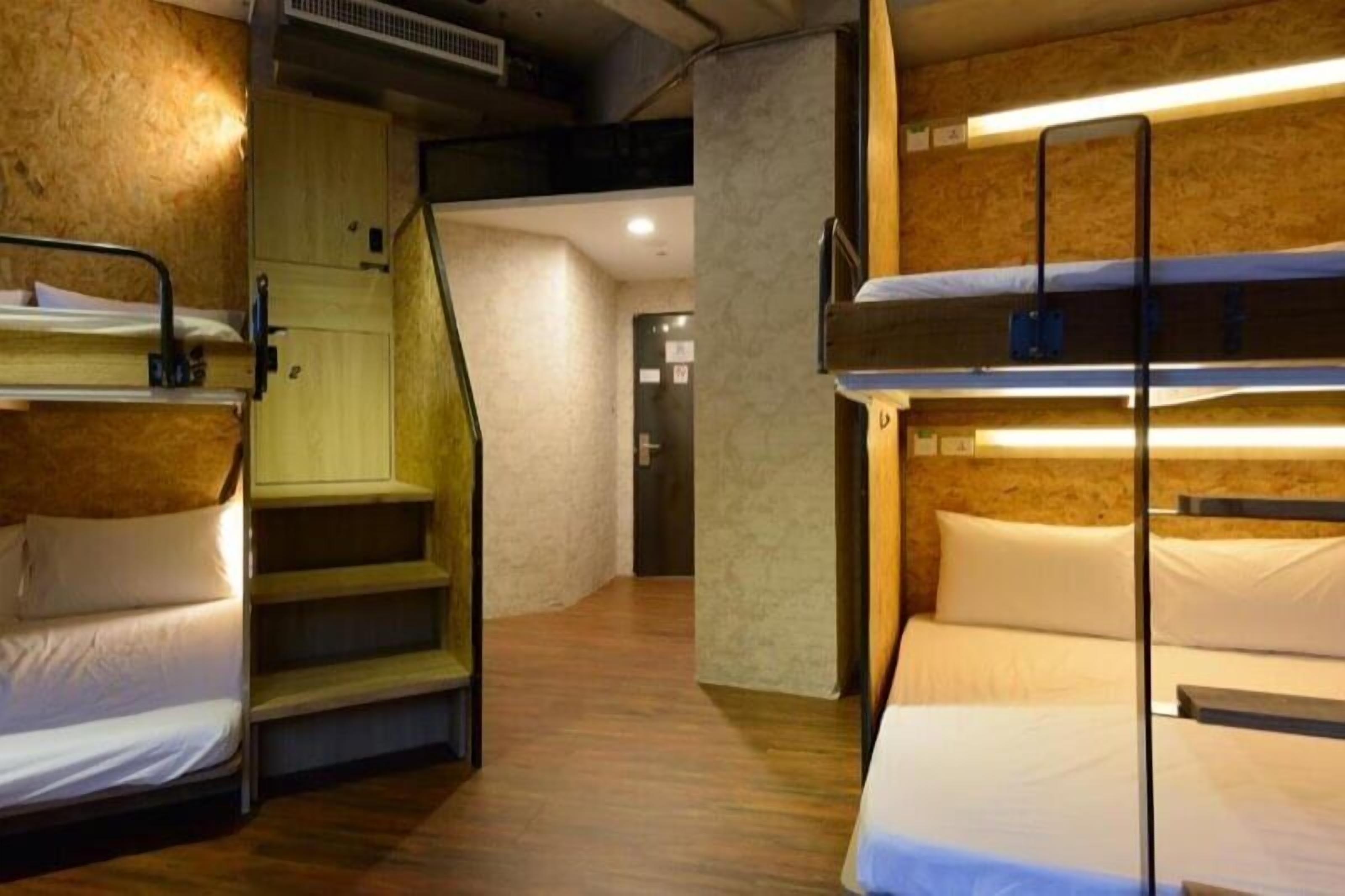 A dormitory-style room with bunk beds, a staircase, and a wooden wall.