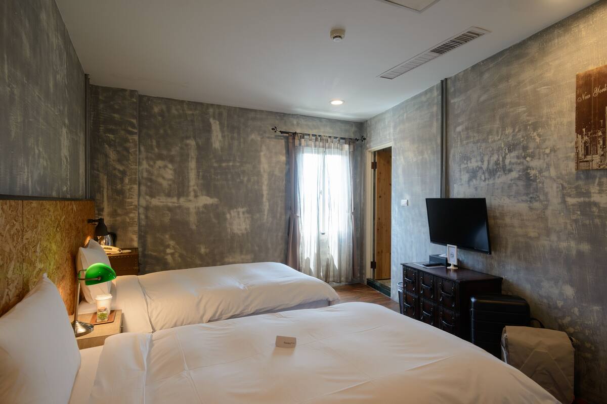 Quarto de hotel com duas camas, televisão, cômoda e janela com cortinas.