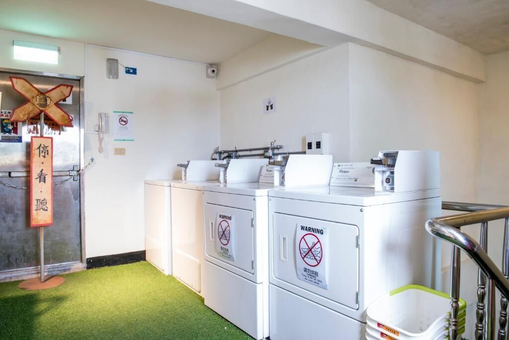 A laundry facility with industrial washing machines, a security camera, and a no-smoking sign.