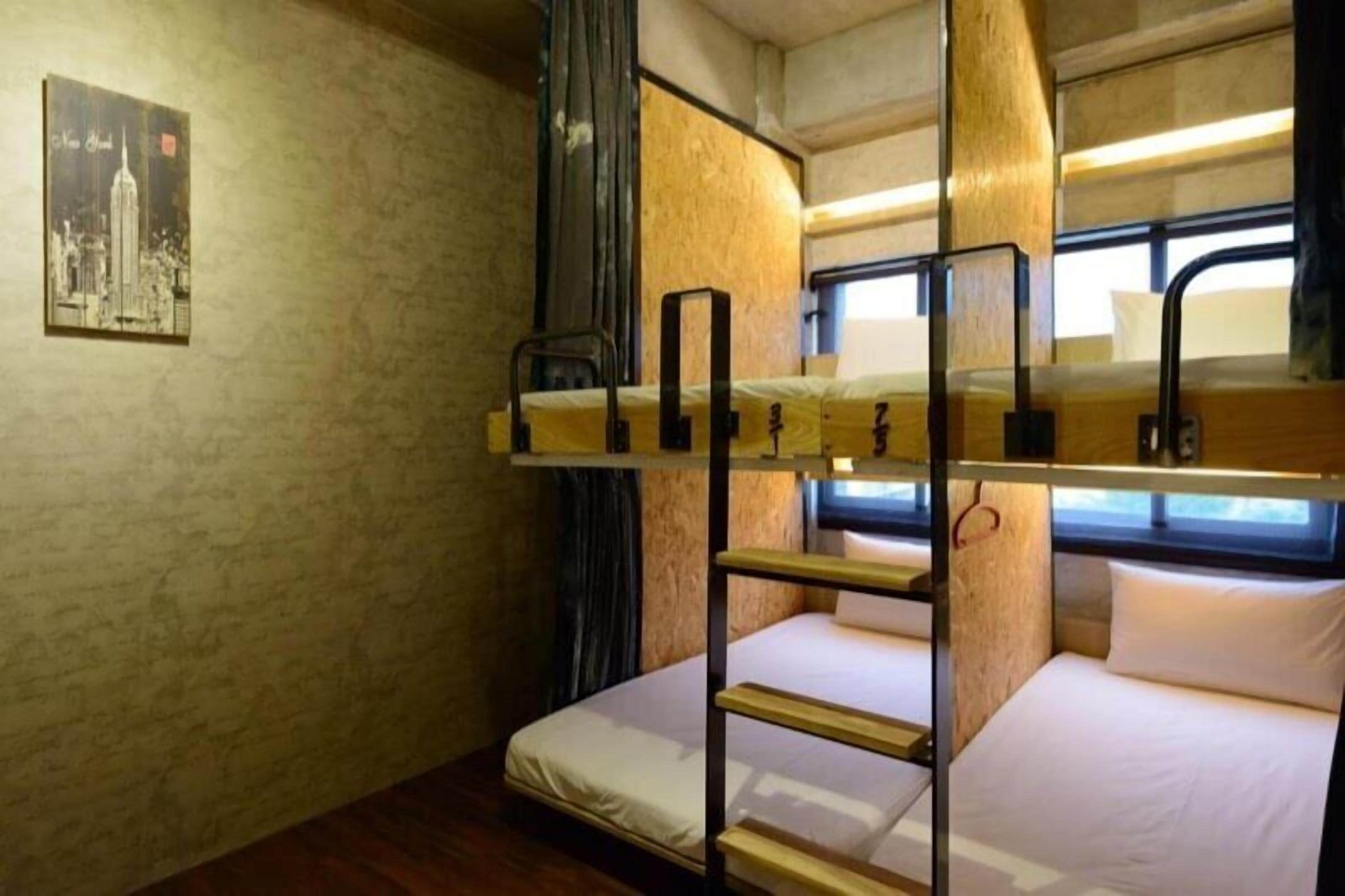 A bunk bed room with a wooden bunk bed, a single bed, a small table, and a wall-mounted shelf.
