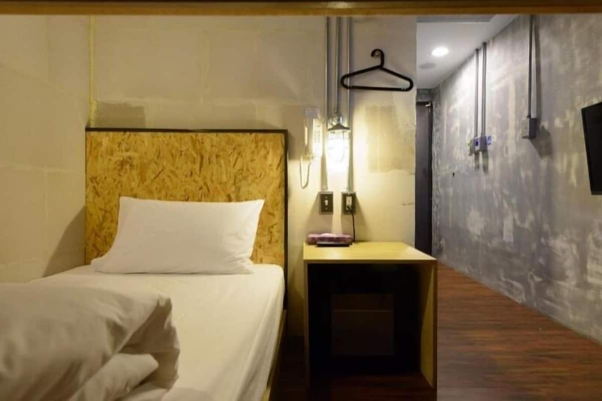 Quarto de hotel com cama, mesa de cabeceira e televisão fixada na parede.