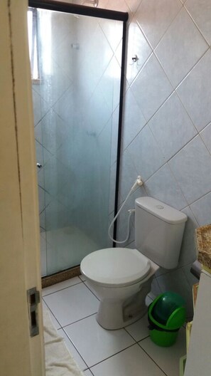 A bathroom with a toilet, a shower enclosure, and a green bucket. - Residencial La Paz (Fortaleza)