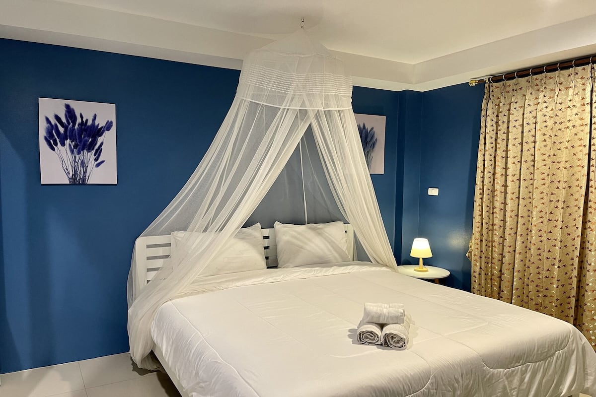 A neatly made bed with a white canopy, a bedside lamp, and a towel on the bed.