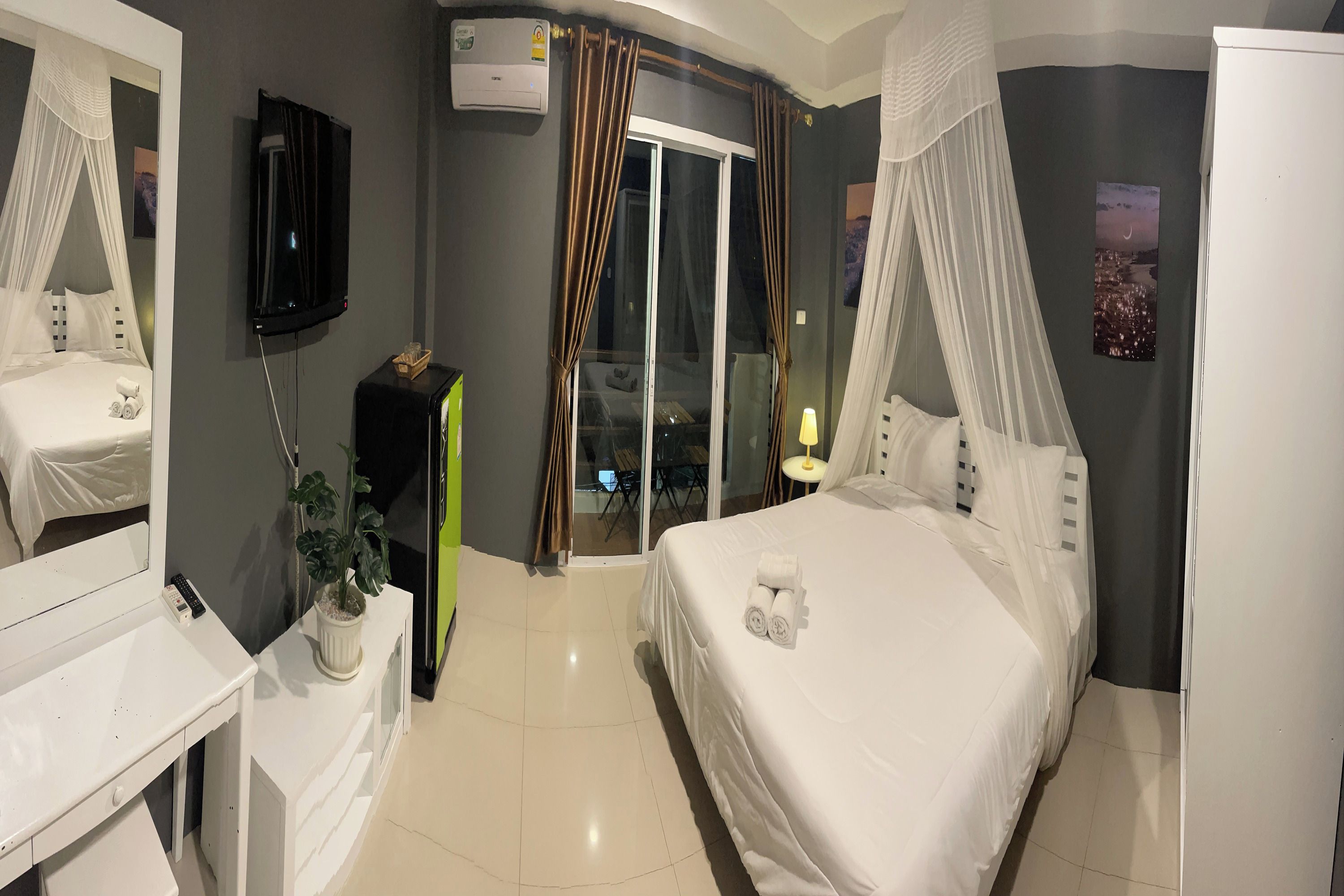 Habitación de hotel con cama, televisión, planta, ventana con cortinas y vistas al exterior.