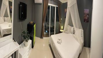 Habitación de hotel con cama, televisión, planta, ventana con cortinas y vistas al exterior.