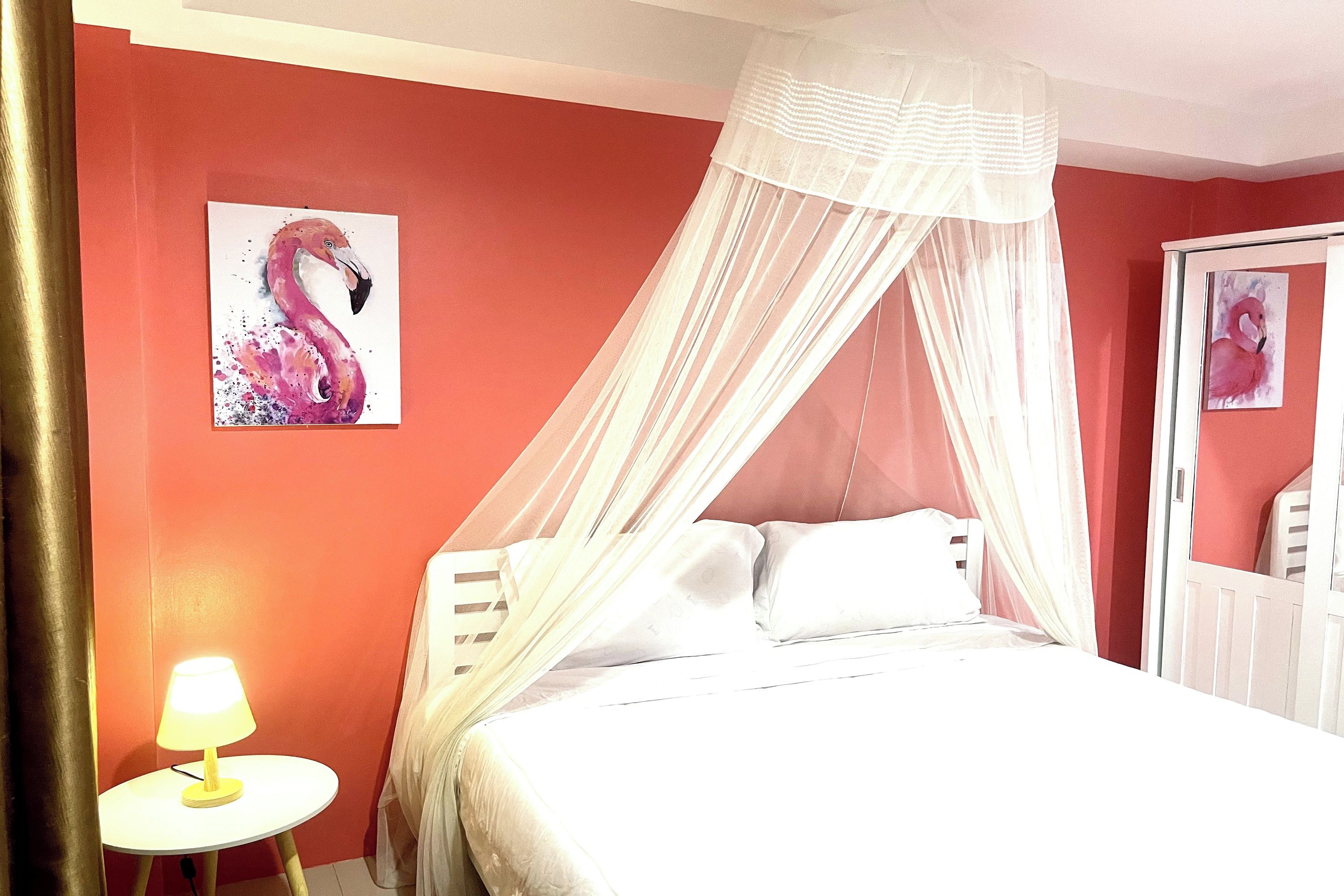 A room with a bed under a canopy, a bedside table with a lamp, and two framed pictures on the wall.
