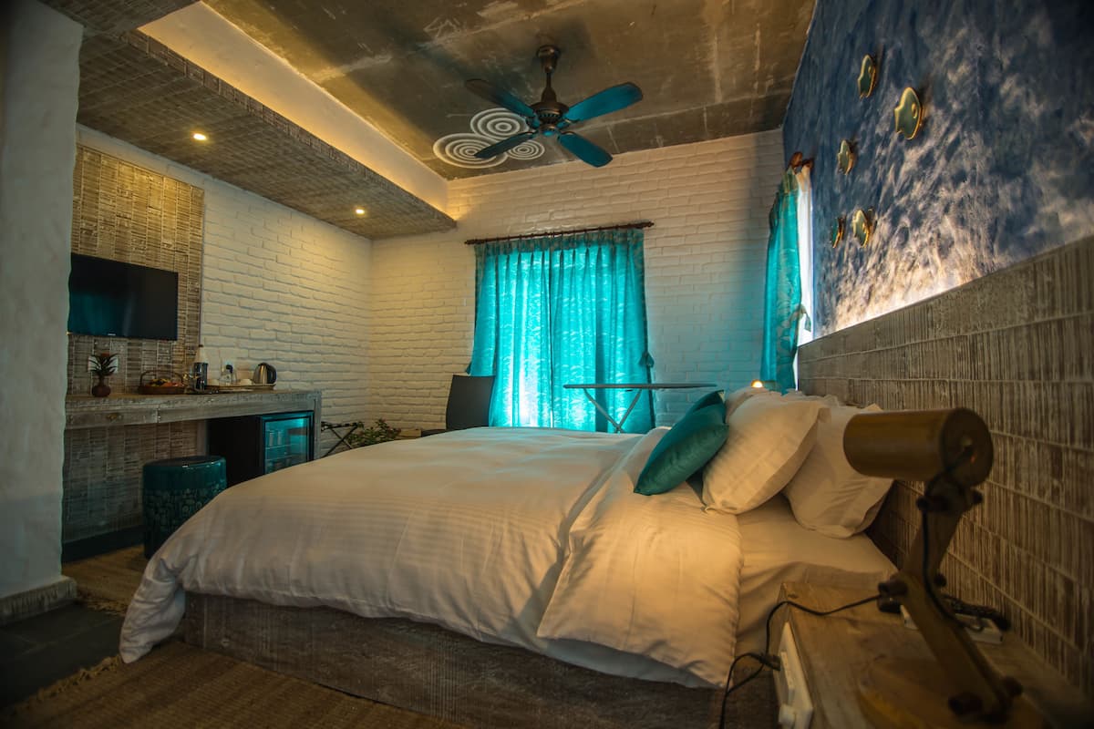 A bedroom with a bed, a desk, a chair, a ceiling fan, and a window with curtains.