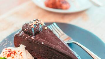 Un plato de postre con pastel de chocolate y crema batida, un tenedor y una taza al fondo.