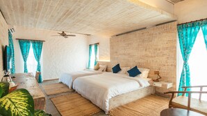 Quarto com duas camas, ventoinha no teto e parede de tijolos rústicos.