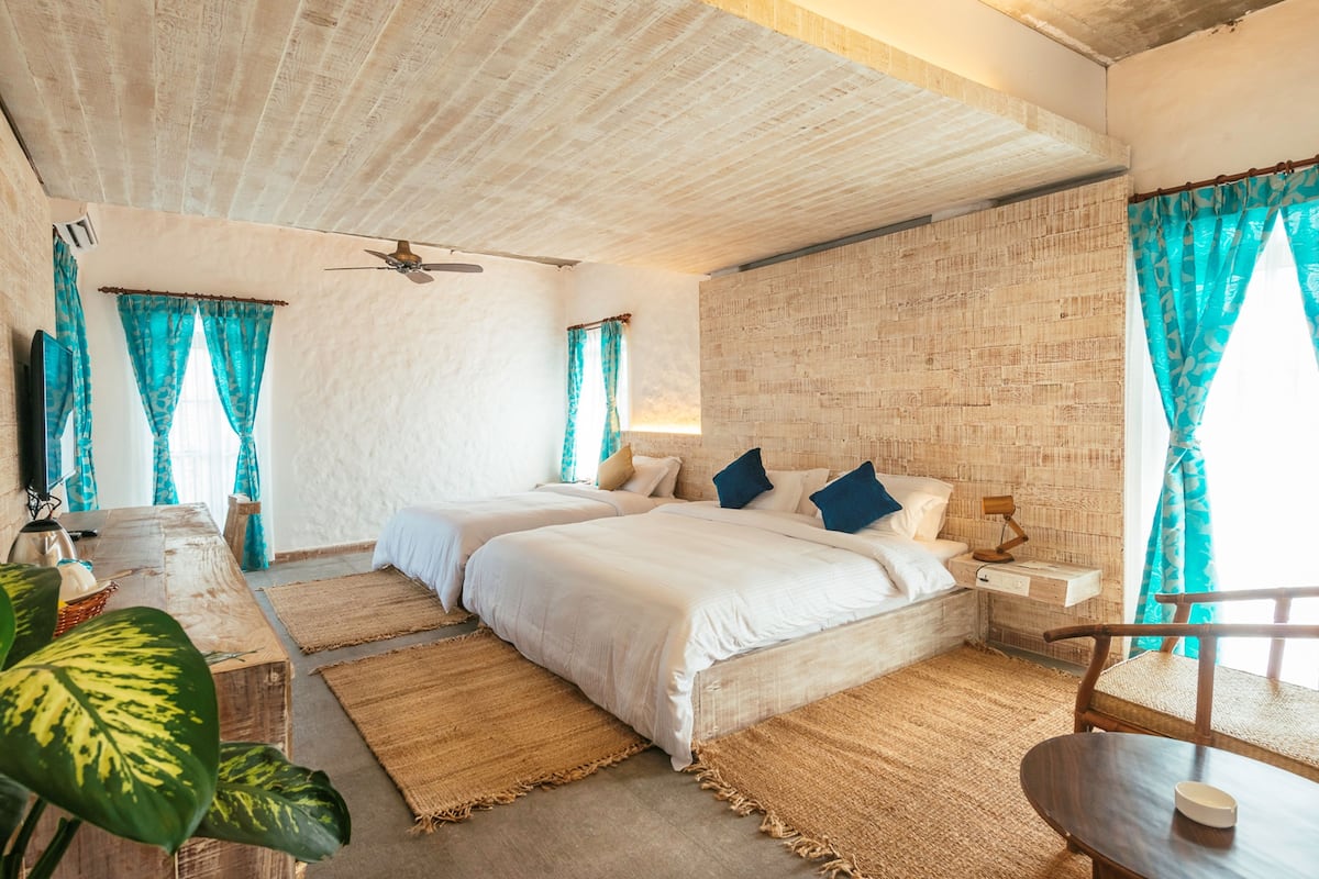 A bedroom with two beds, a ceiling fan, and a rustic brick wall.