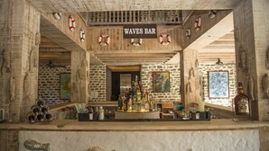 Uma área de bar com uma placa que diz "WAVES BAR", rodeada por paredes de pedra e decorações náuticas.