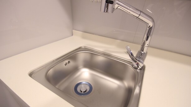 A stainless steel kitchen sink with a modern faucet and a blue drain cover. - WA Hotel Nampo (Busan)