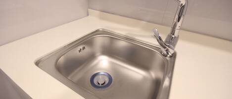 Un lavamanos de acero inoxidable con un grifo moderno y un tapón de desagüe azul.