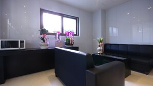 Un salon moderne avec un canapé noir, une table basse et un four à micro-ondes posé sur un plan de travail noir. Une fenêtre offre une vue sur l’extérieur, et un vase rempli de fleurs est posé sur le plan de travail.