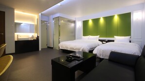 Une chambre d’hôtel avec deux lits, un canapé, une table basse, une salle de bain avec un miroir et un petit bureau.