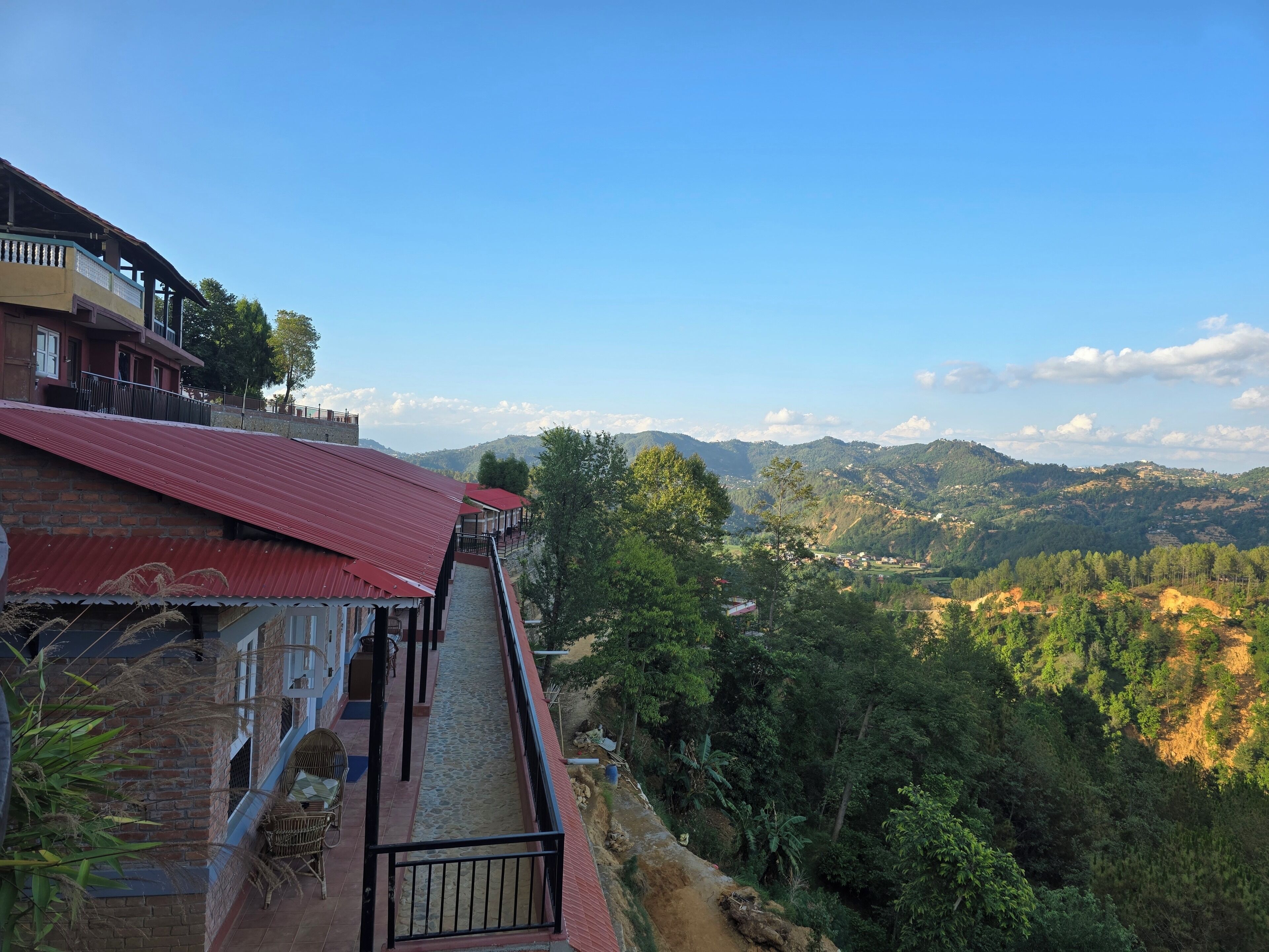 A building with a red roof, a stone staircase, and a view of a mountainous landscape.