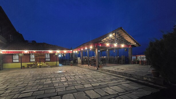 A stone-paved courtyard with a covered seating area and a building with a sign. - Balthali Village Resort (Balthali)