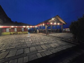 A stone-paved courtyard with a covered seating area and a building with a sign. - Balthali Village Resort (Balthali)