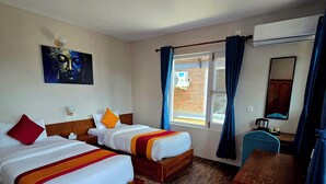 A hotel room with two beds, a wooden floor, a large window with curtains, a desk, and a wall-mounted air conditioner. - Balthali Village Resort (Balthali)