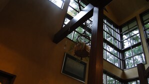 Een kamer met hoge plafonds, grote ramen, houten balken en hangende lampen.