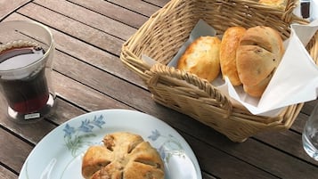 A wooden table with a plate of food, a basket of bread, a glass of beverage, and a candle.