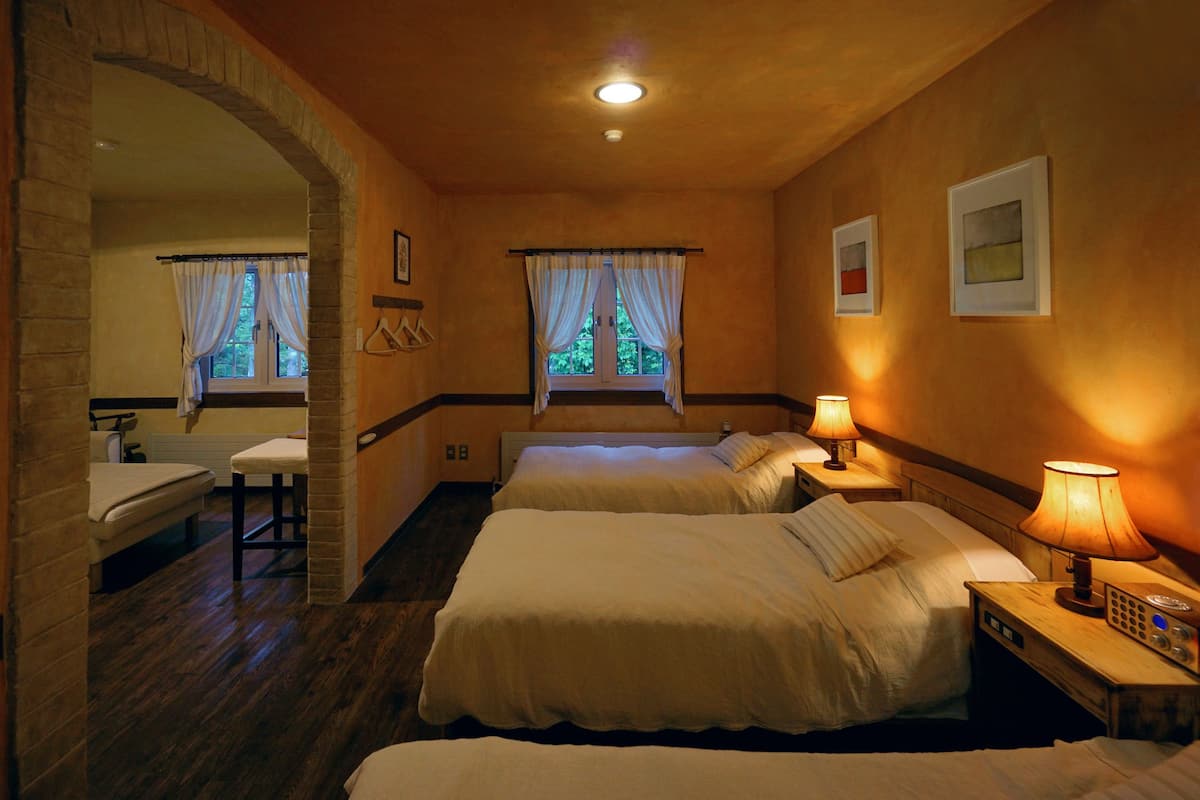 Ein Hotelzimmer mit zwei Betten, einer Sitzecke mit einer Bank, einem Fenster mit Vorhängen und einem Nachttisch mit Lampe.