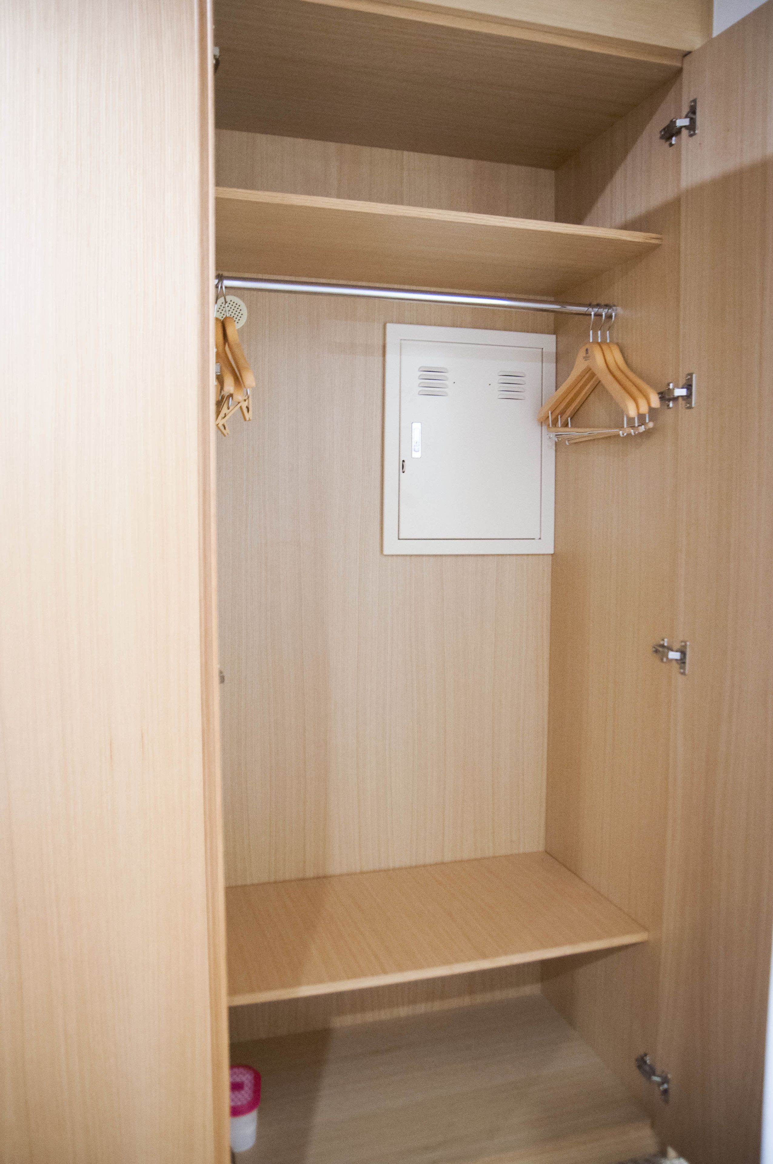 A wooden closet with a metal rod for hanging clothes and a small white cabinet.