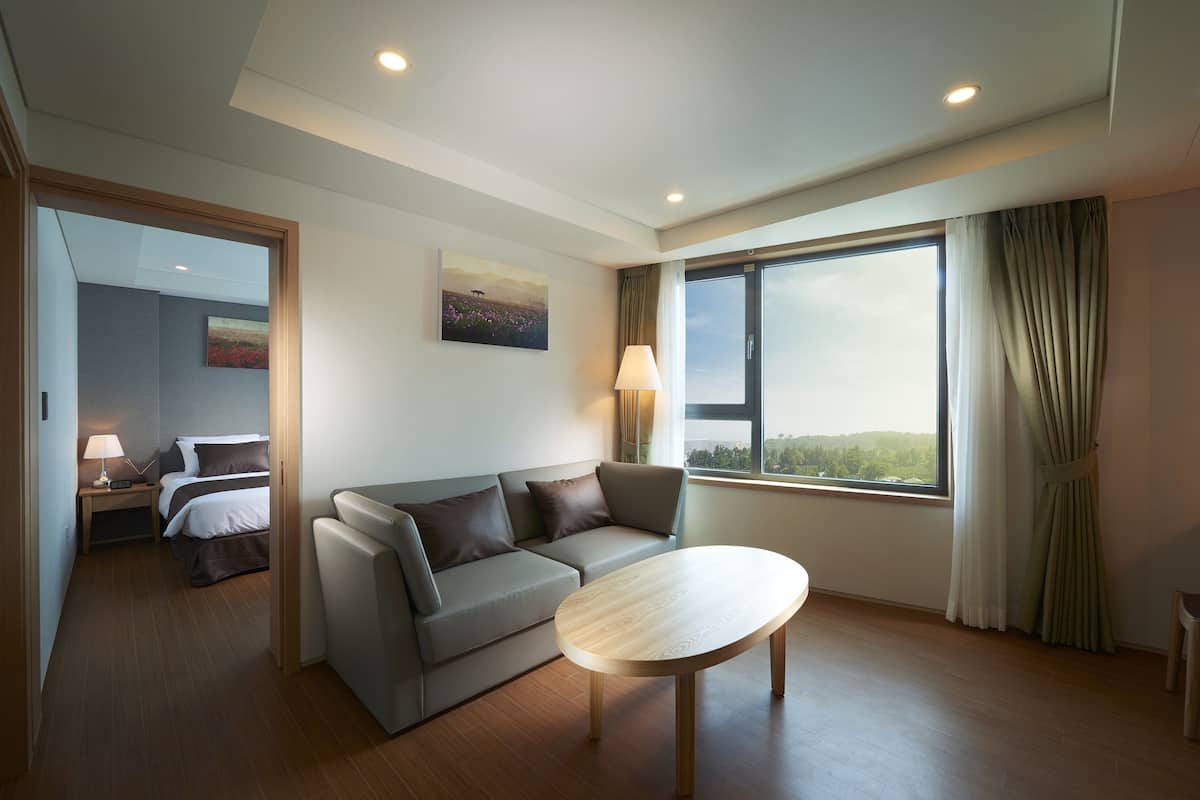 A modern hotel room with a sofa, a round table, and a large window offering a view of the outdoors.