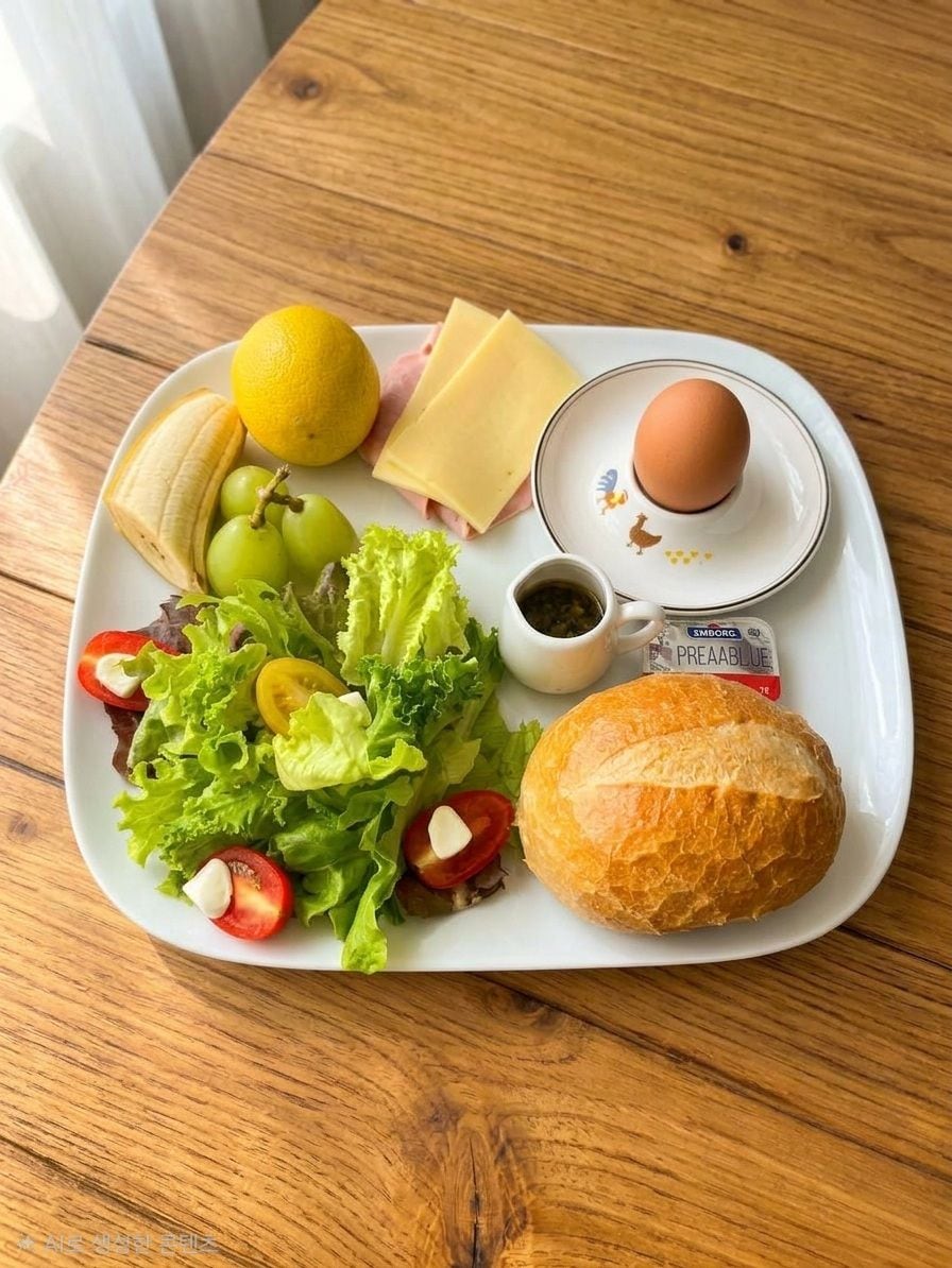 A meal tray with a sandwich, a slice of cheese, a boiled egg, a lemon, grapes, a small salad, and a baguette.