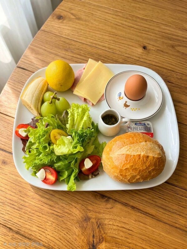 A meal tray with a sandwich, a slice of cheese, a boiled egg, a lemon, grapes, a small salad, and a baguette.