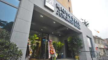 Welcome to Jungmuan Hotel, featuring a modern entrance with lush greenery and the hotel's name prominently displayed.