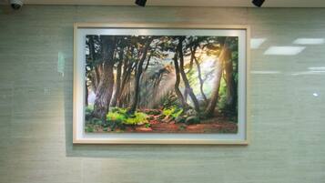 A room with a framed forest painting, two orange chairs, a small table, and a ceiling-mounted light fixture.