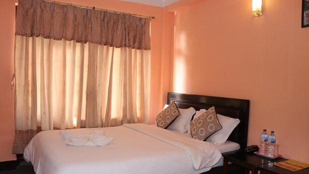 A neatly made bed with white linens, a wooden headboard, and decorative pillows. There is a nightstand with a lamp and bottled water. - Hotel Hana (Kathmandu)