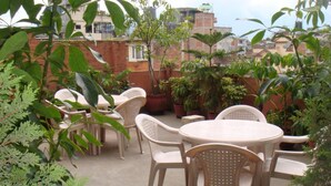 An outdoor patio with round tables and chairs, surrounded by potted plants and greenery. - Hotel Hana (Kathmandu)