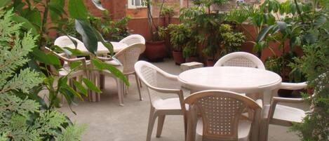 An outdoor patio with round tables and chairs, surrounded by potted plants and greenery.