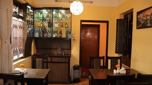 A bar area with a variety of bottles, a wooden counter, and a hanging light fixture. There are tables and chairs arranged for dining. - Hotel Hana (Kathmandu)