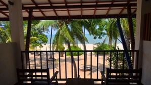 A balcony with two wooden chairs and a table, overlooking a sandy beach with palm trees and the ocean. - Wellé Wadiya (Kudawa)