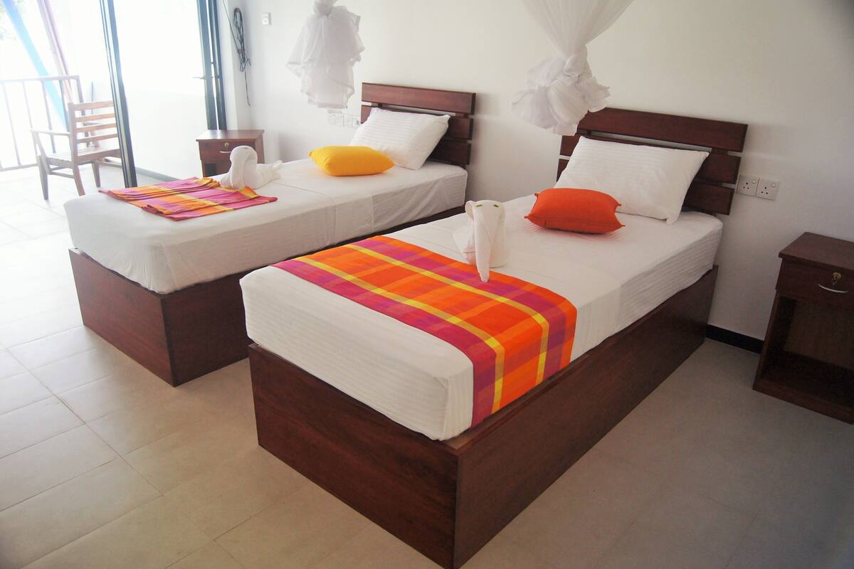 A hotel room with two beds, each with a wooden headboard, white bedding, and colorful blankets.
