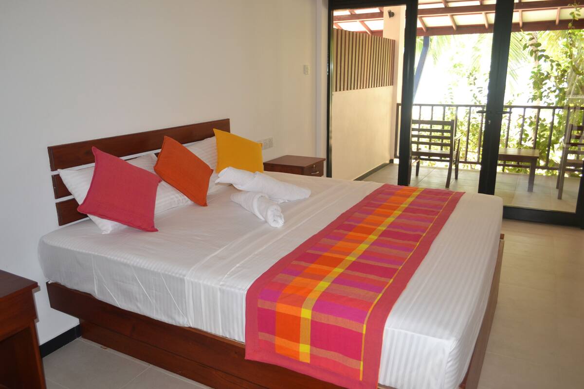 A neatly made bed with a white mattress, a colorful striped blanket, and several pillows in red, orange, and yellow.