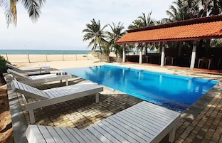 Área da piscina com espreguiçadeiras, espaço de estar coberto e vista para a praia.