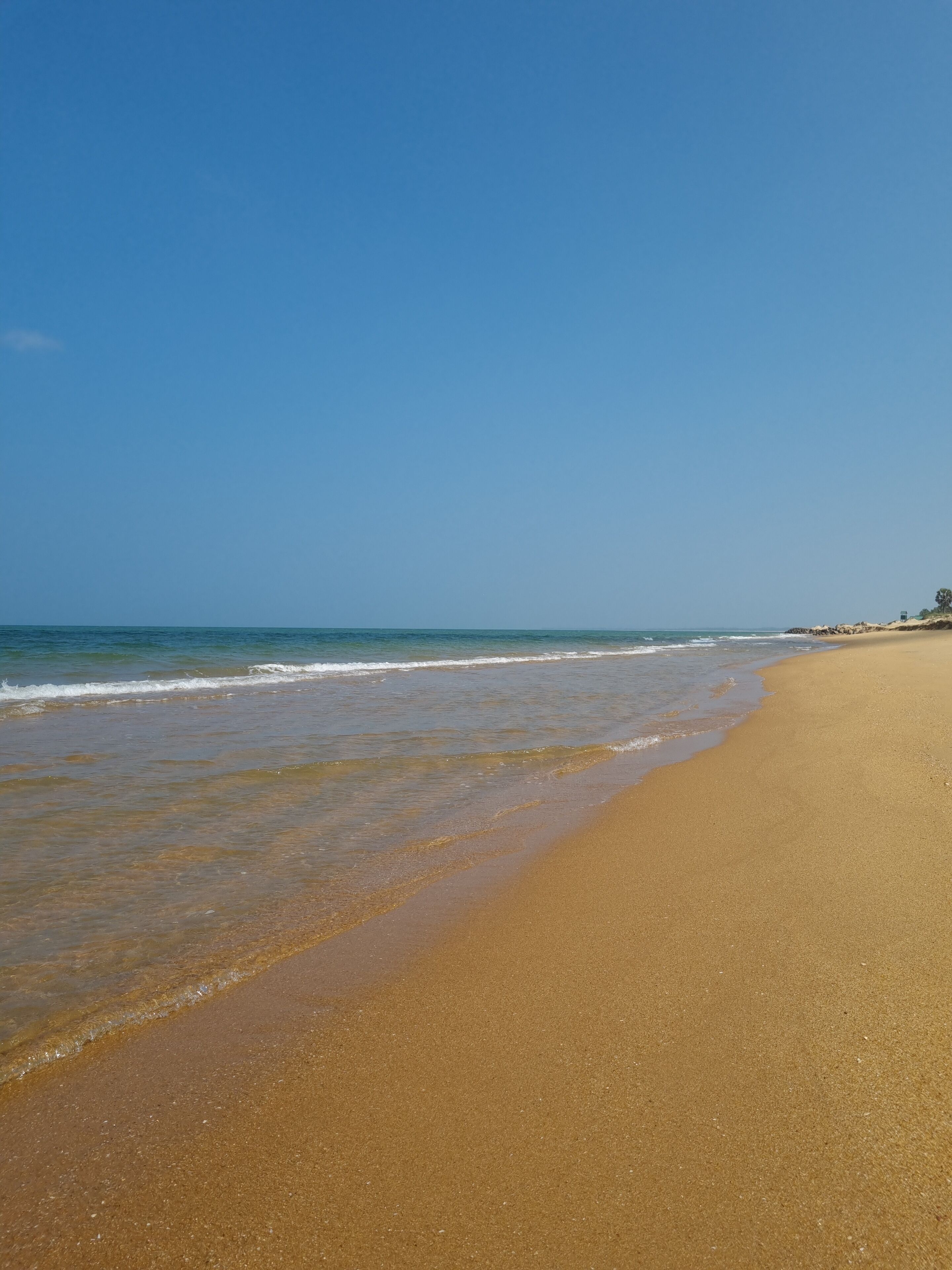 Una extensa playa arenosa con olas suaves y un cielo azul despejado.