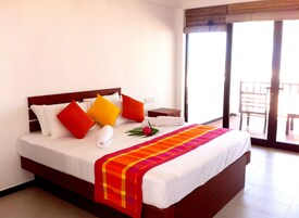 Quarto de hotel com uma cama grande, cabeceira de madeira e varanda com uma cadeira.