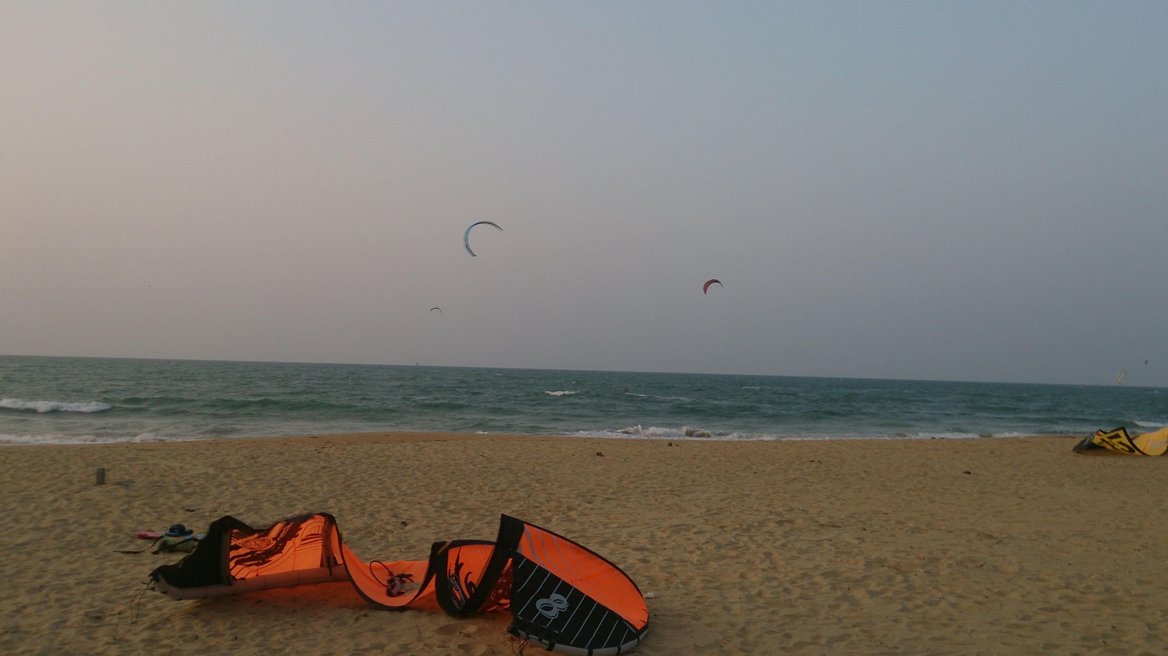 A beach with a kite and a surfboard on the sand.