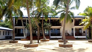 A multi-story building with a flat roof, surrounded by palm trees and open spaces. - Wellé Wadiya (Kudawa)