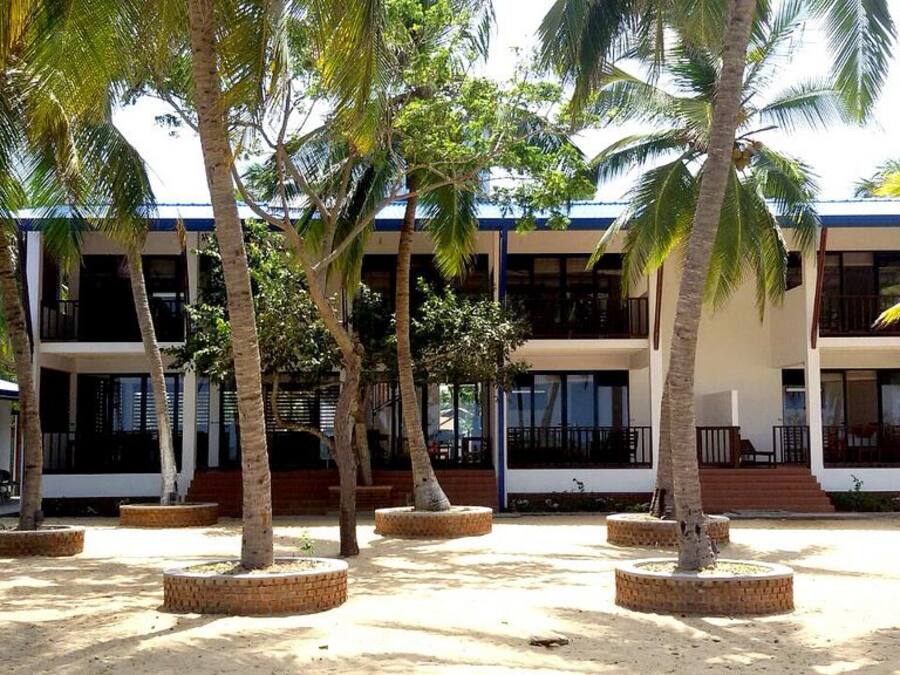 A multi-story building with a flat roof, surrounded by palm trees and open spaces.