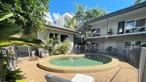 A swimming pool with a brick border, surrounded by a fenced area with a chair and a building in the background. - Cairns City Motel (Cairns)