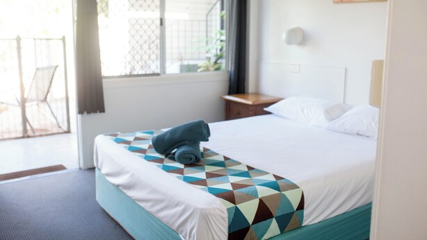 A hotel room with a bed, a window, a nightstand, and a chair. - Cairns City Motel (Cairns)