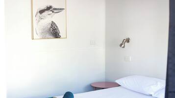 A hotel room with a bed, a small bedside table, a wall-mounted light, a ceiling fan, and a framed picture on the wall.